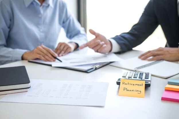 A financial adviser discussing retirement planning with a client while reviewing documents and financial calculations.
